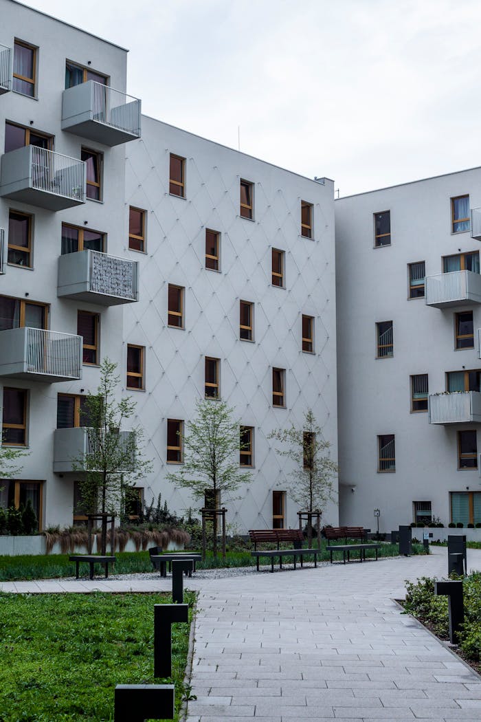 hero-img-02 Contemporary white urban apartment buildings with balconies and greenery.