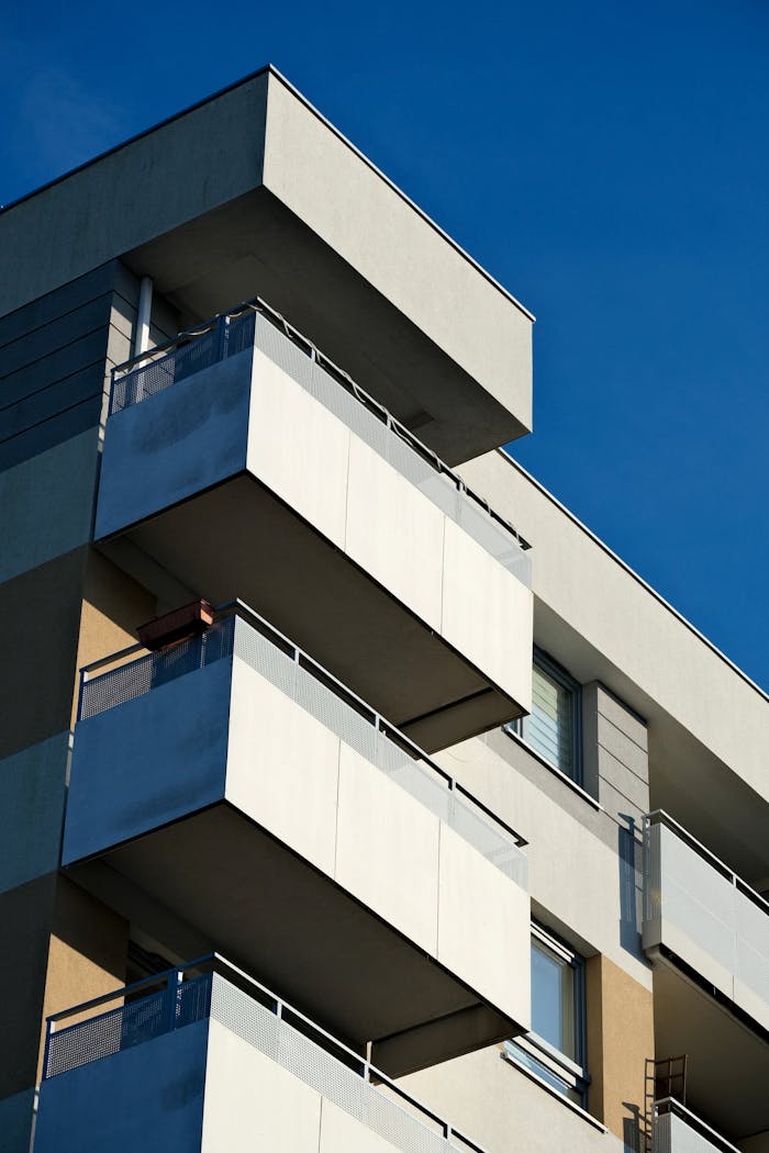 why-choose-us Close-up of a modern apartment building showcasing minimalist design against a clear blue sky.